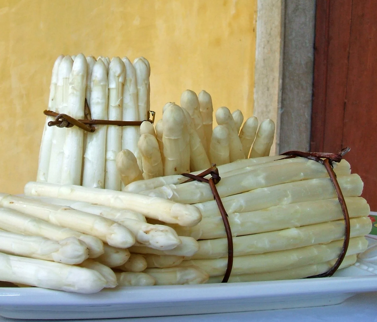 Mazzi di asparagi bianchi di Bassano legati con rametti di salice, su un piatto bianco