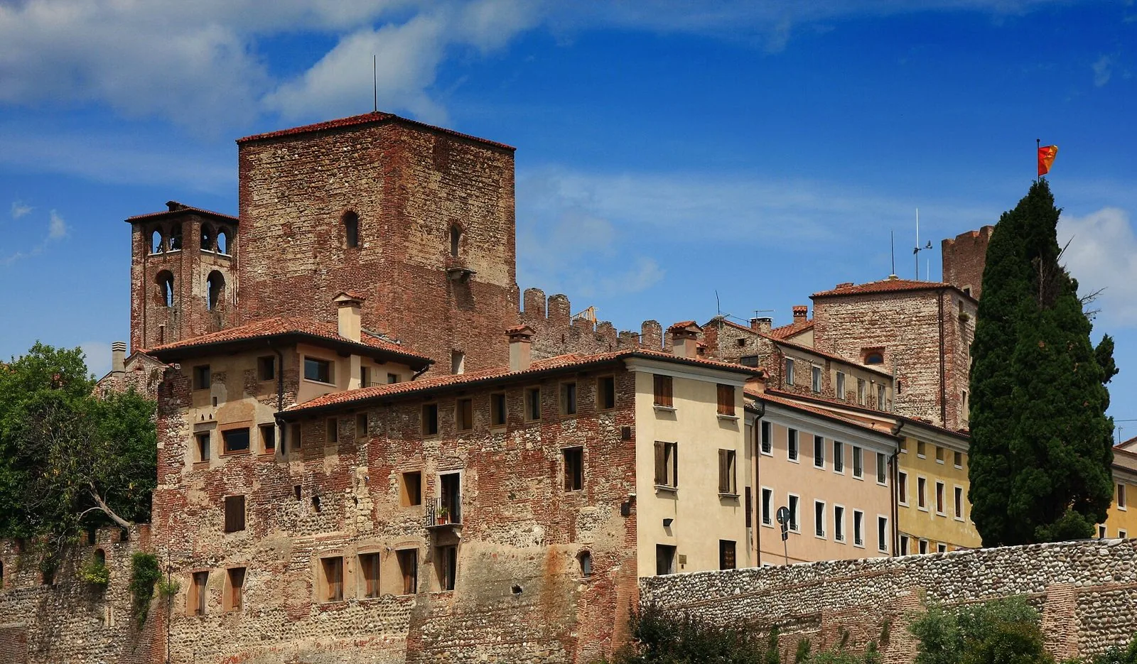 Le torri in pietra e mattoni del Castello degli Ezzelini a Bassano del Grappa, con le case del centro storico e un cipresso sotto un cielo azzurro