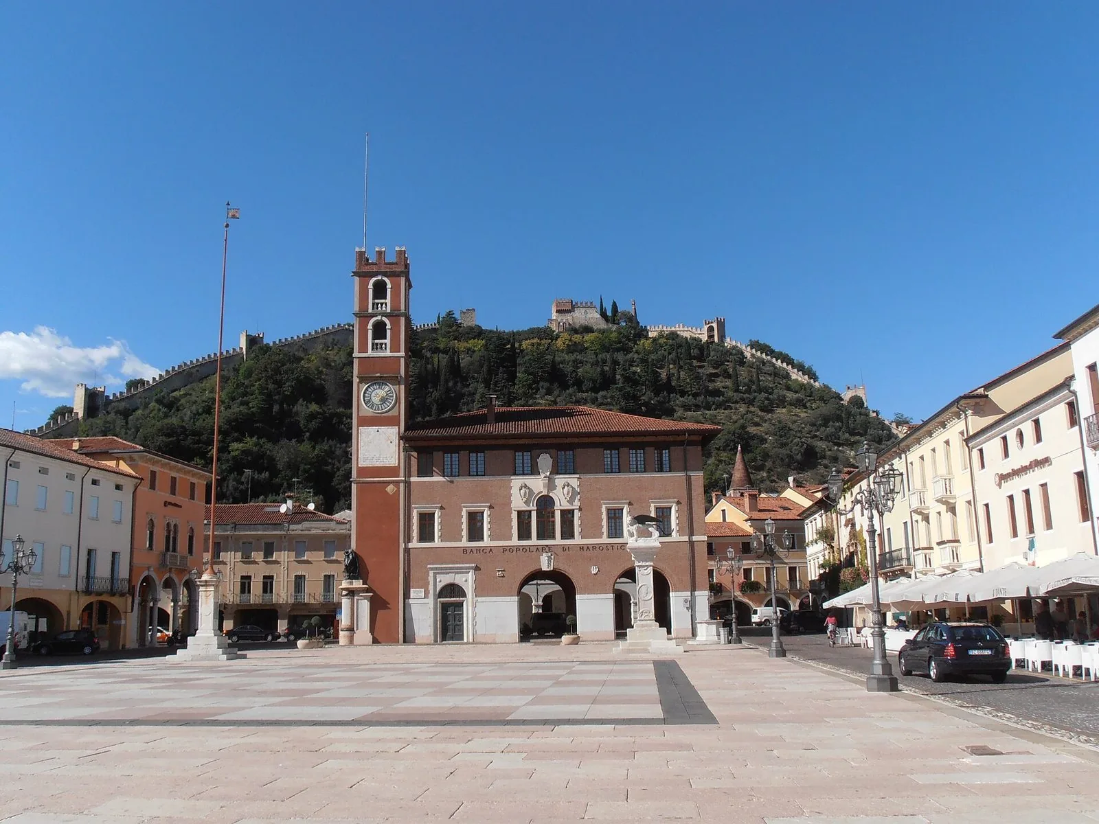 Piazza degli Scacchi a Marostica con la torre dell'orologio e il palazzo porticato; sul colle alle spalle, le mura merlate e il Castello Superiore