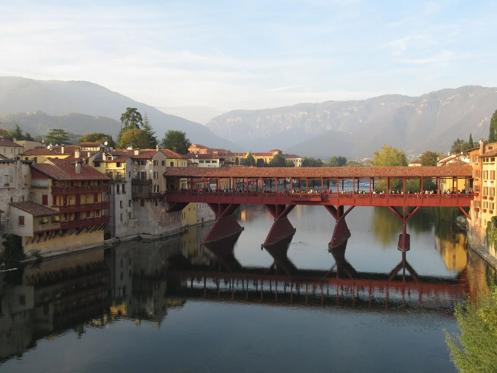 Il Ponte Vecchio di Bassano del Grappa, ponte coperto in legno rosso sul fiume Brenta, con le case affacciate sull'acqua e le montagne sullo sfondo